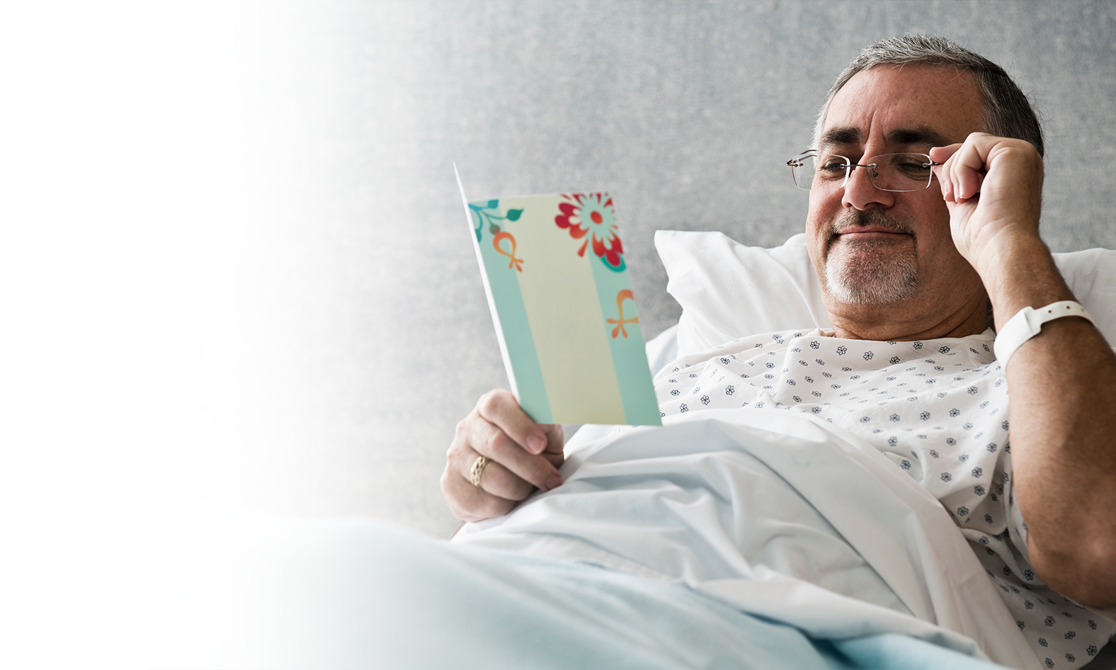 Man in hospital bed reading card smiling